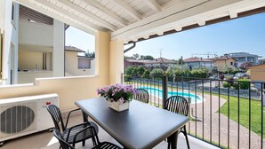 Een balkon met een tafel, stoelen, een bloevas en uitzicht op het zwembad.