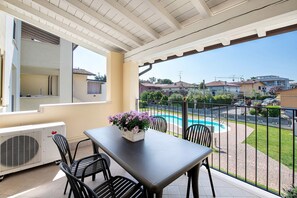 Een balkon met een tafel, stoelen, een bloevas en uitzicht op het zwembad.