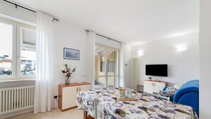 Een moderne kamer met een eettafel, stoelen, een televisie en uitzicht naar buiten.