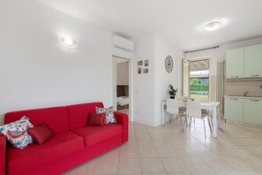 Een moderne woonkamer met een rode bank, een eethoek met een tafel en stoelen, en een keuken met lichtgroene kastjes.