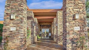 A stone building entrance with 'VENU' signs, a covered walkway, and a glass door leading inside. - Indigo-Communal Pool, Hot Tub, Gym & Movie Theater (Scottsdale)