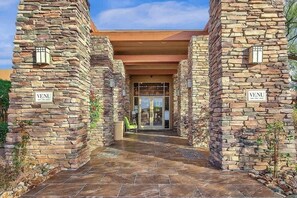 A stone building entrance with 'VENU' signs, a covered walkway, and a glass door leading inside. - Indigo-Communal Pool, Hot Tub, Gym & Movie Theater (Scottsdale)