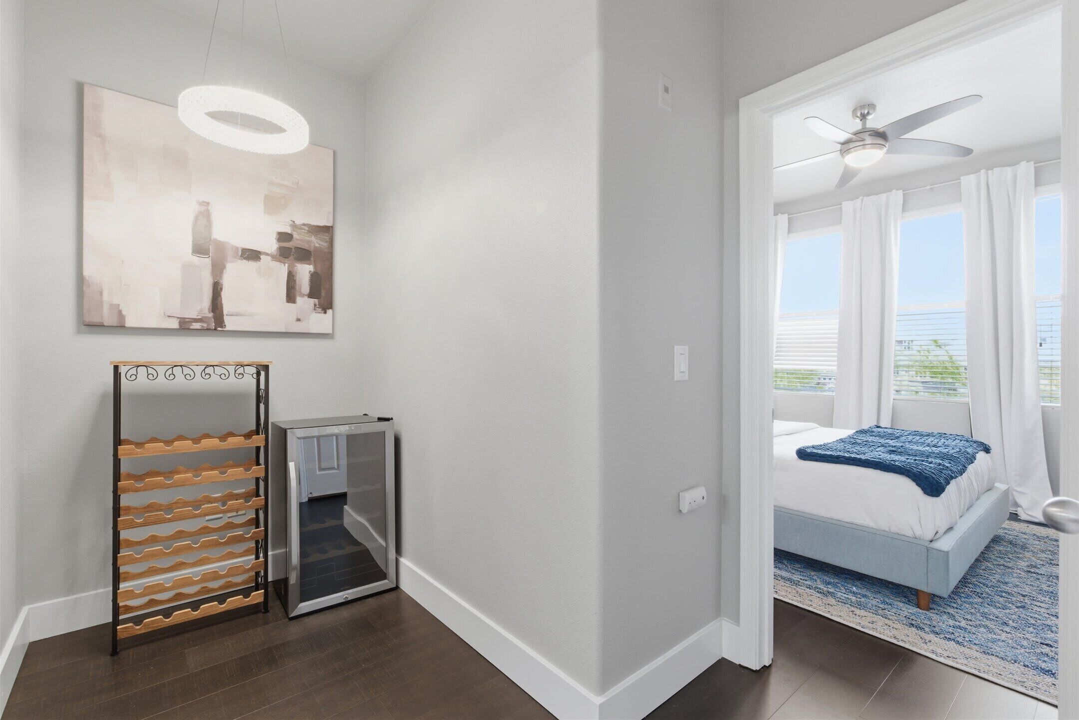 A bedroom with a bed, a ceiling fan, a window with curtains, and a wall-mounted artwork.