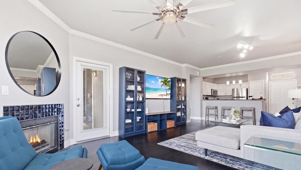 A modern living room with a fireplace, blue furniture, a glass coffee table, and a kitchen area with white cabinets and a stainless steel refrigerator. - Indigo-Communal Pool, Hot Tub, Gym & Movie Theater (Scottsdale)