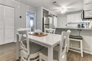 A white dining table with four chairs, a kitchen with white cabinets and appliances, and a ceiling fan. - 'folly Tides' HHI Condo w/ Beach, Pools & Tennis! (Hilton Head Island)
