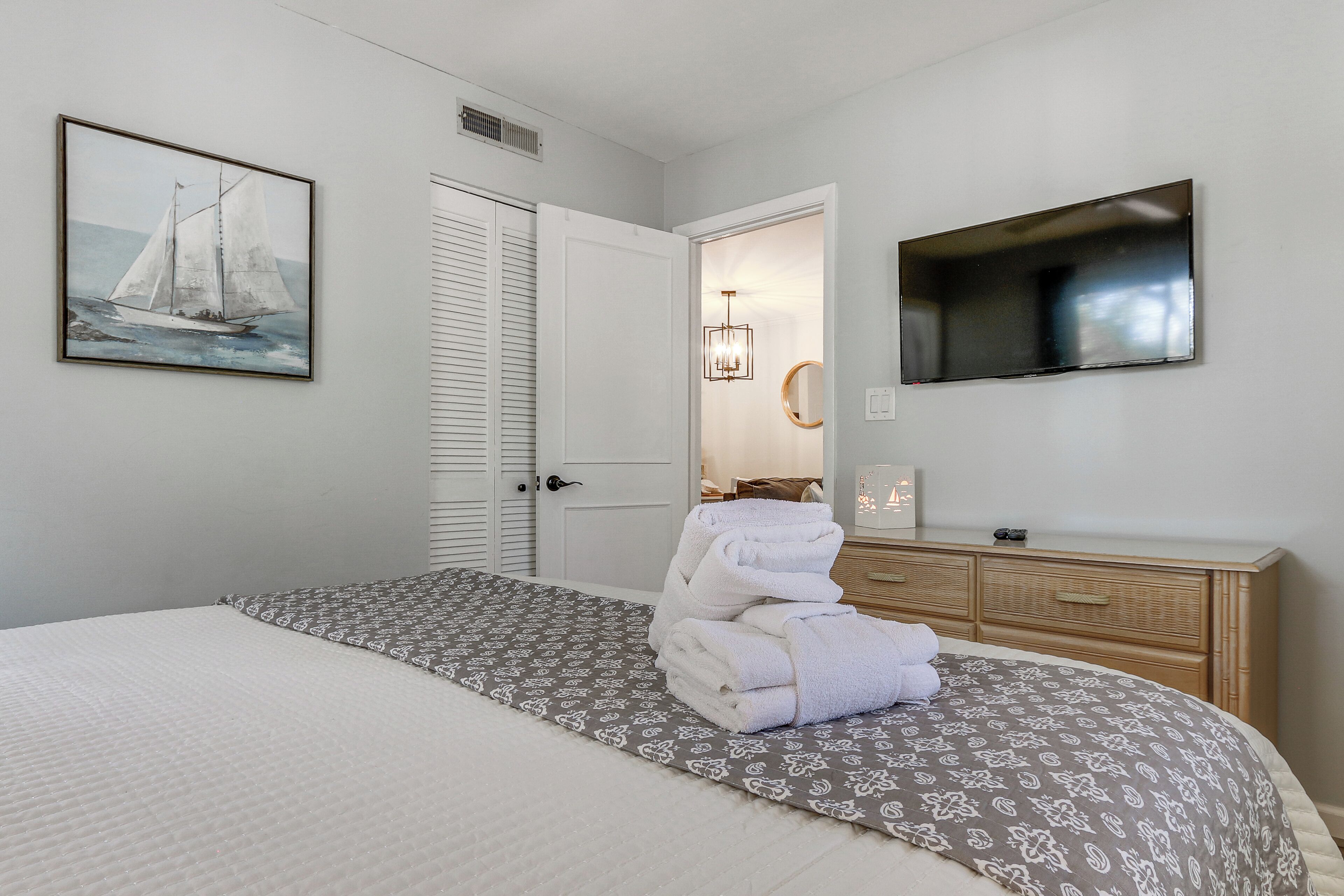 A bedroom with a bed, a painting, a television, and a bathroom door.
