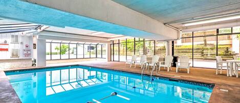 An indoor swimming pool with clear water, white chairs, and tables around the pool area.
