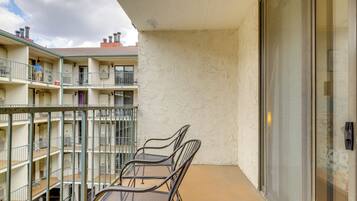 A balcony with metal chairs and a table, a glass door, and a view of a multi-story building with balconies.
