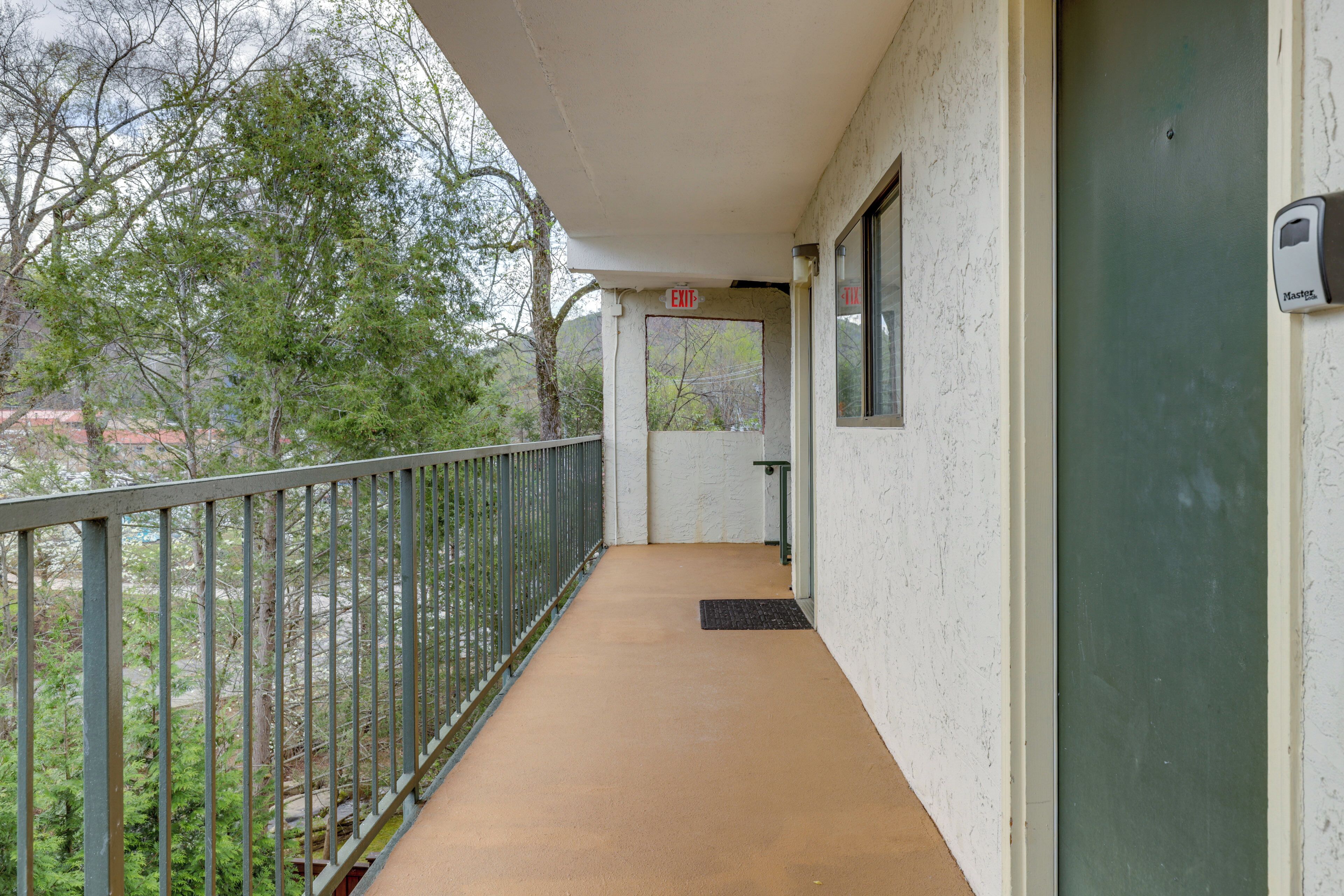 A balcony with a metal railing, a door with an 'EXIT' sign, and a view of trees and buildings.