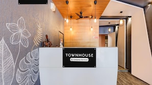 Un comptoir d’accueil avec une enseigne indiquant « TOWNHOUSE, services d’entreprise », un ventilateur de plafond, des luminaires suspendus et un mur en bois orné de motifs de feuilles.