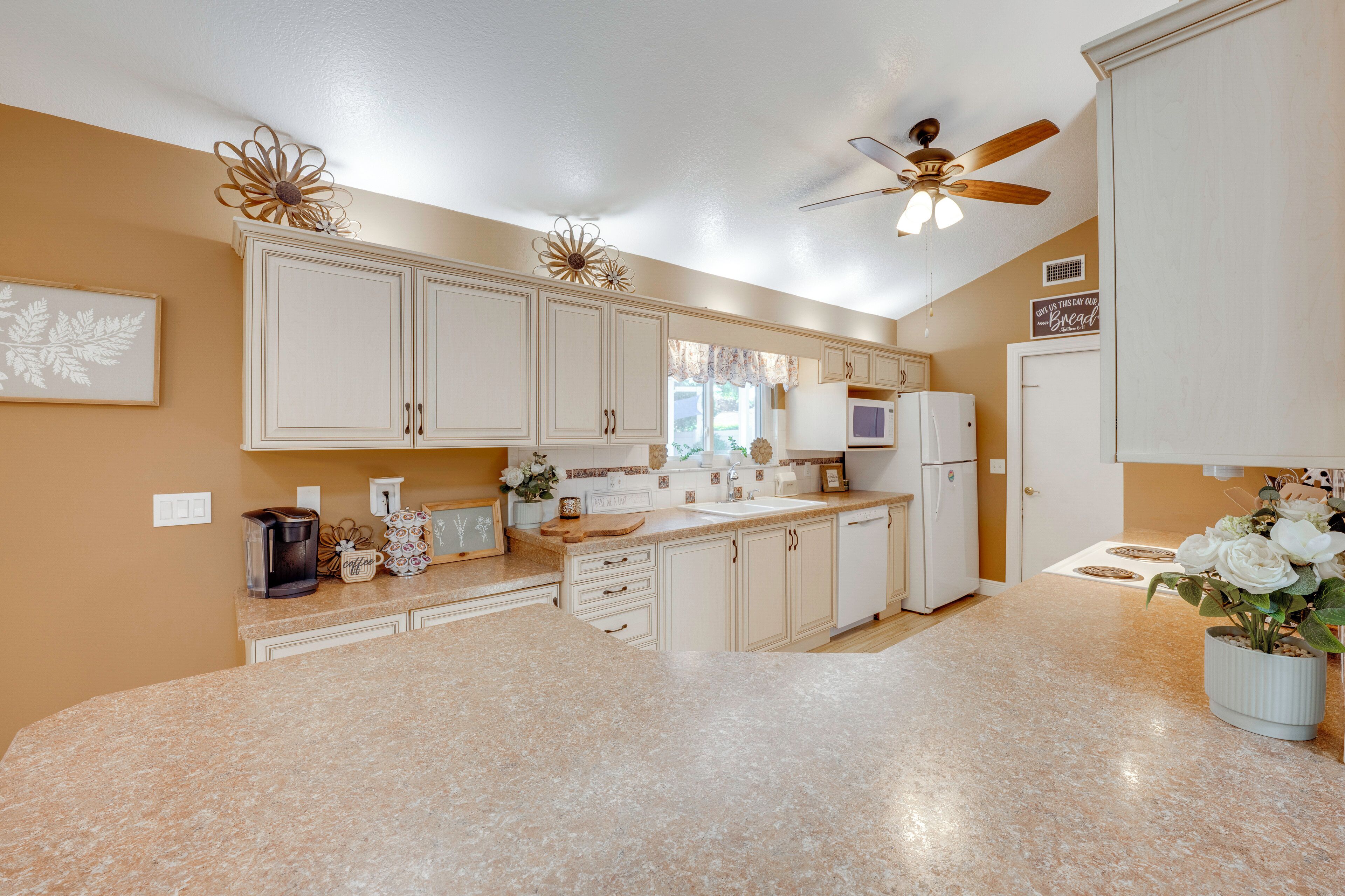 A kitchen with white cabinets, a granite countertop, a ceiling fan, and a potted plant.