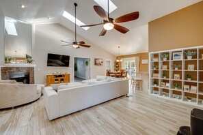 Un salon moderne avec un canapé d’angle, des ventilateurs de plafond, une cheminée, un téléviseur et une bibliothèque.