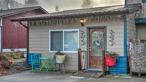 Une petite maison avec une porte d’entrée, une fenêtre, une véranda avec une chaise et un jardinière.