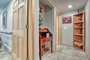Un couloir avec une porte en bois, une petite table avec des tiroirs, une étagère ornée d’objets décoratifs et un tableau accroché au mur.