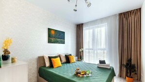 Een slaapkamer met een bed, een schilderij, een raam met gordijnen, een nachtkastje en een potplant.