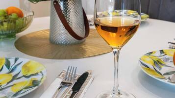 Una mesa de comedor con una copa de vino blanco, un jarrón con flores y un cuenco de fruta.