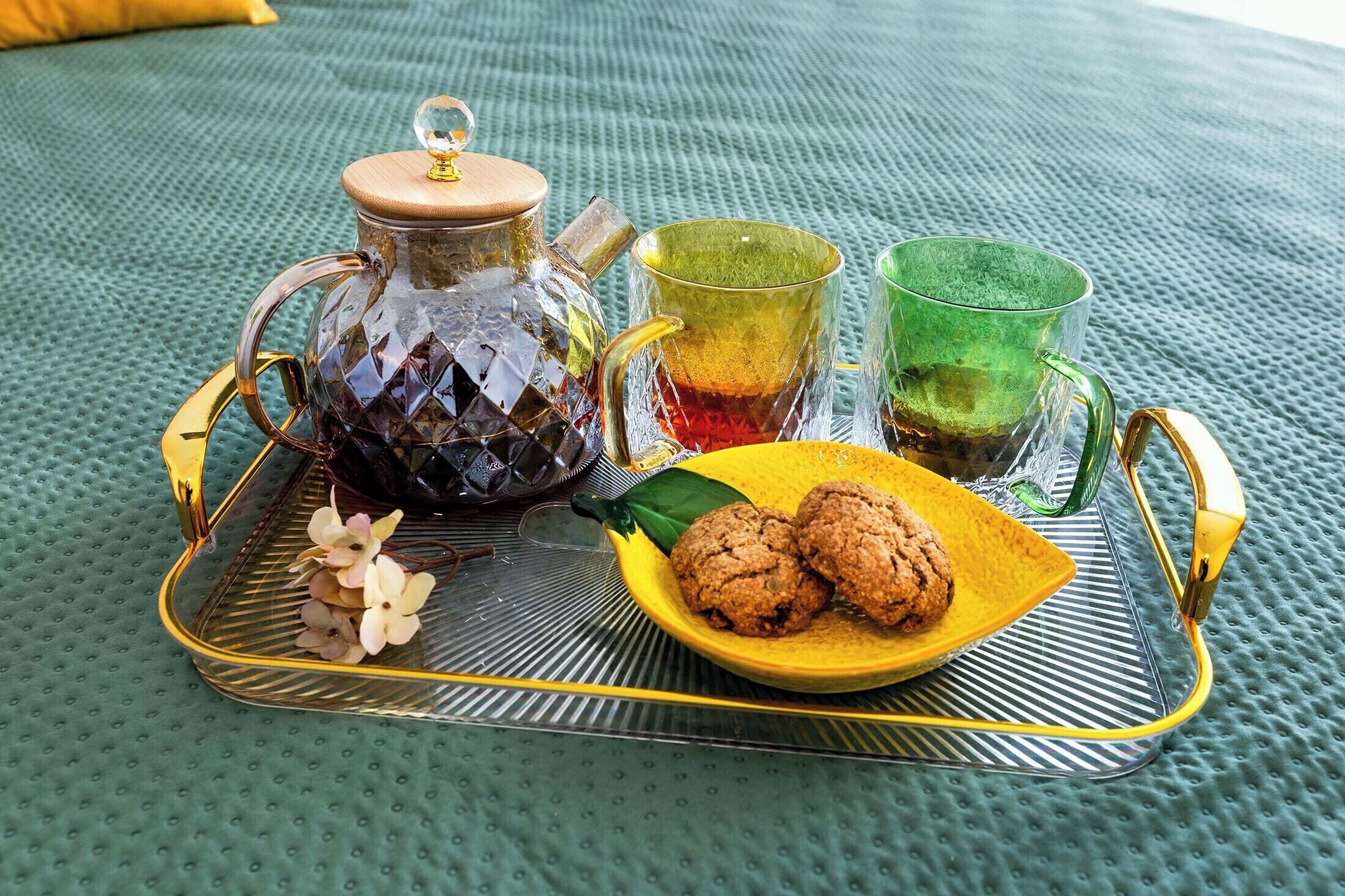 Una bandeja con una tetera de vidrio, dos vasos, un plato de galletas y un pequeño adorno.