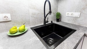 Een keuken met een zwarte spoelbak, twee groene borden met peren, een potplant en een marmeren achterwand.