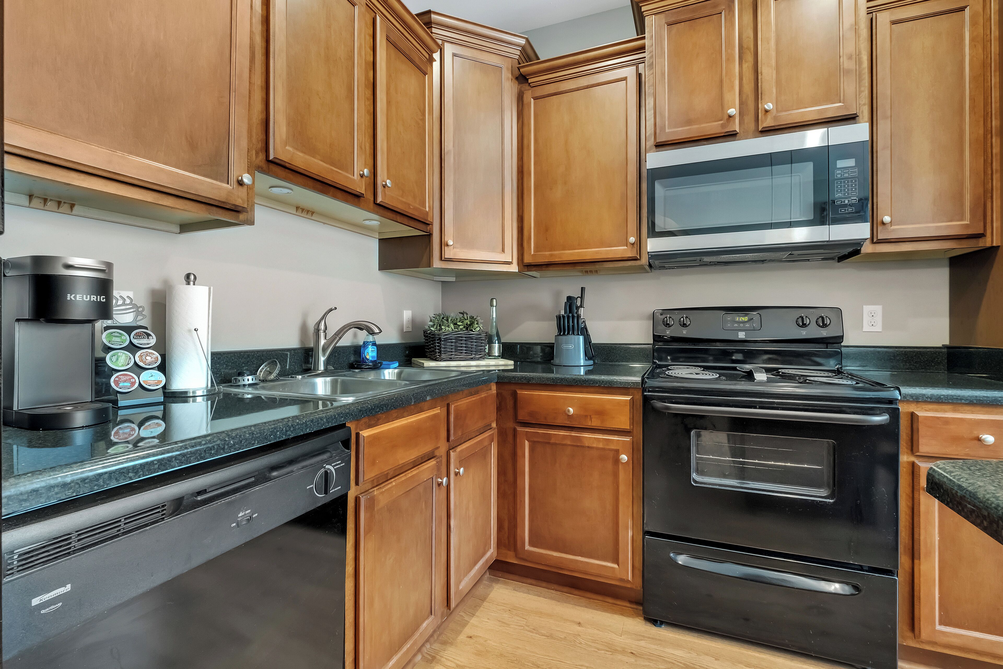 A kitchen with wooden cabinets, a stainless steel microwave, a black stove, and a coffee maker.