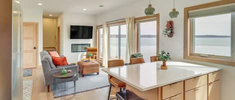 Una cocina moderna con una isla grande, un área de comedor con sillas, un sofá y un televisor montado en la pared.
