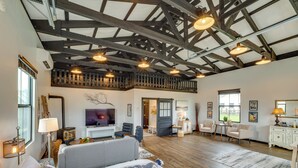 Una habitación amplia con techo alto, vigas de madera, una cama grande, un televisor y un comedor con sillas y una mesa.