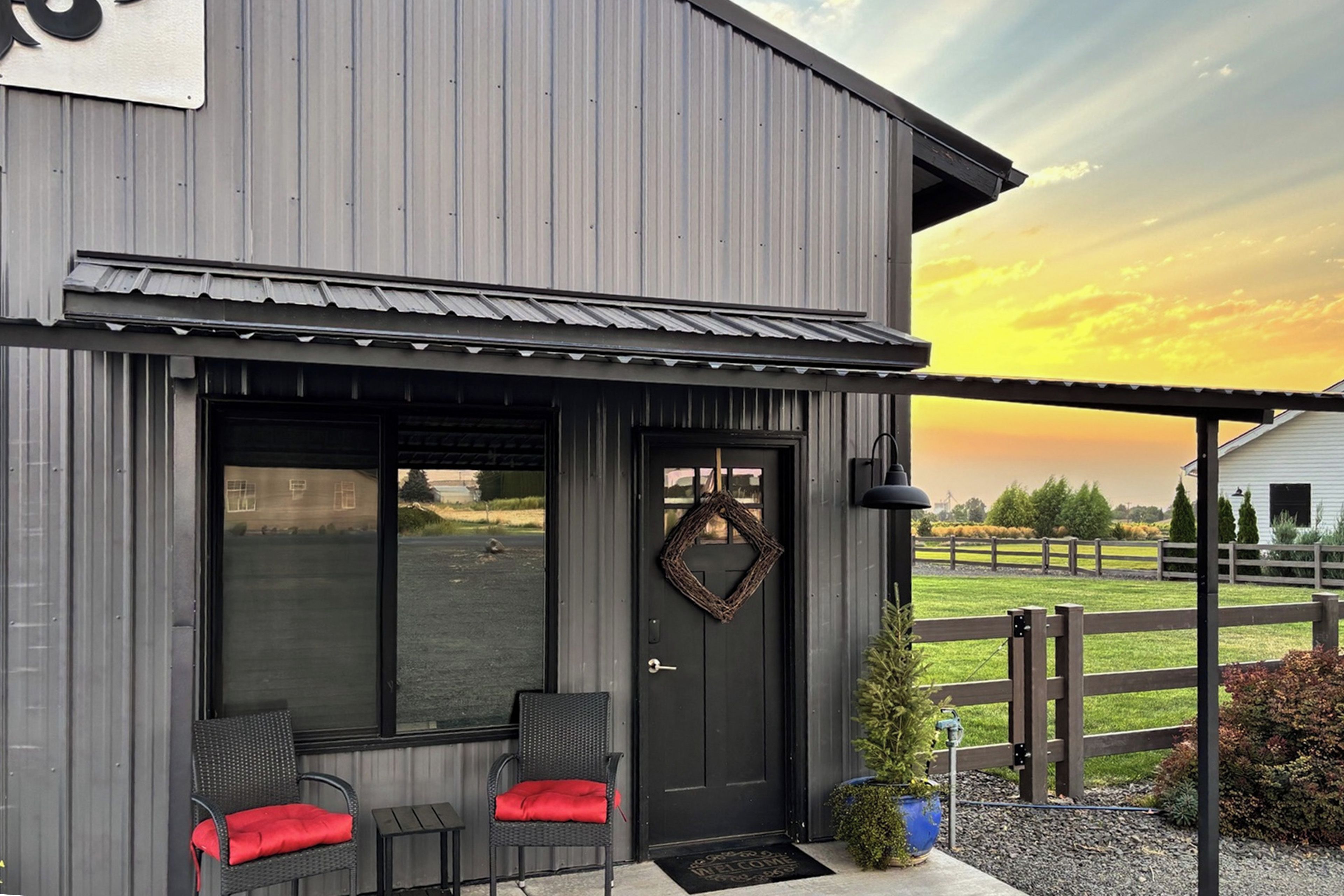 A modern building with a dark exterior, a welcoming entrance with a door and a window, and a small outdoor seating area with two chairs.