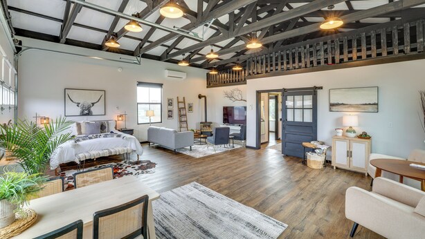 Una habitación amplia con techo alto, vigas a la vista, una cama, un sofá, una mesa de comedor y una escalera.