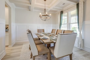 A dining room with a long table, chairs, a chandelier, and large windows with curtains.