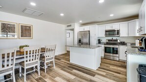 A modern kitchen with white cabinets, a built-in microwave, stainless steel appliances, and a wooden dining table with chairs. - Explore Gila Valley & Eac! Modern Thatcher Home (Thatcher)