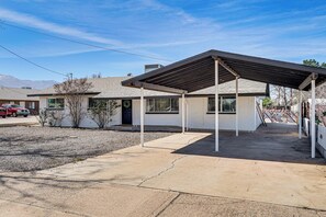 A single-story house with a covered patio, a gravel driveway, and a mountain backdrop.