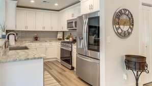 Cozinha moderna com armários brancos, eletrodomésticos de aço inoxidável e um relógio de parede decorativo.
