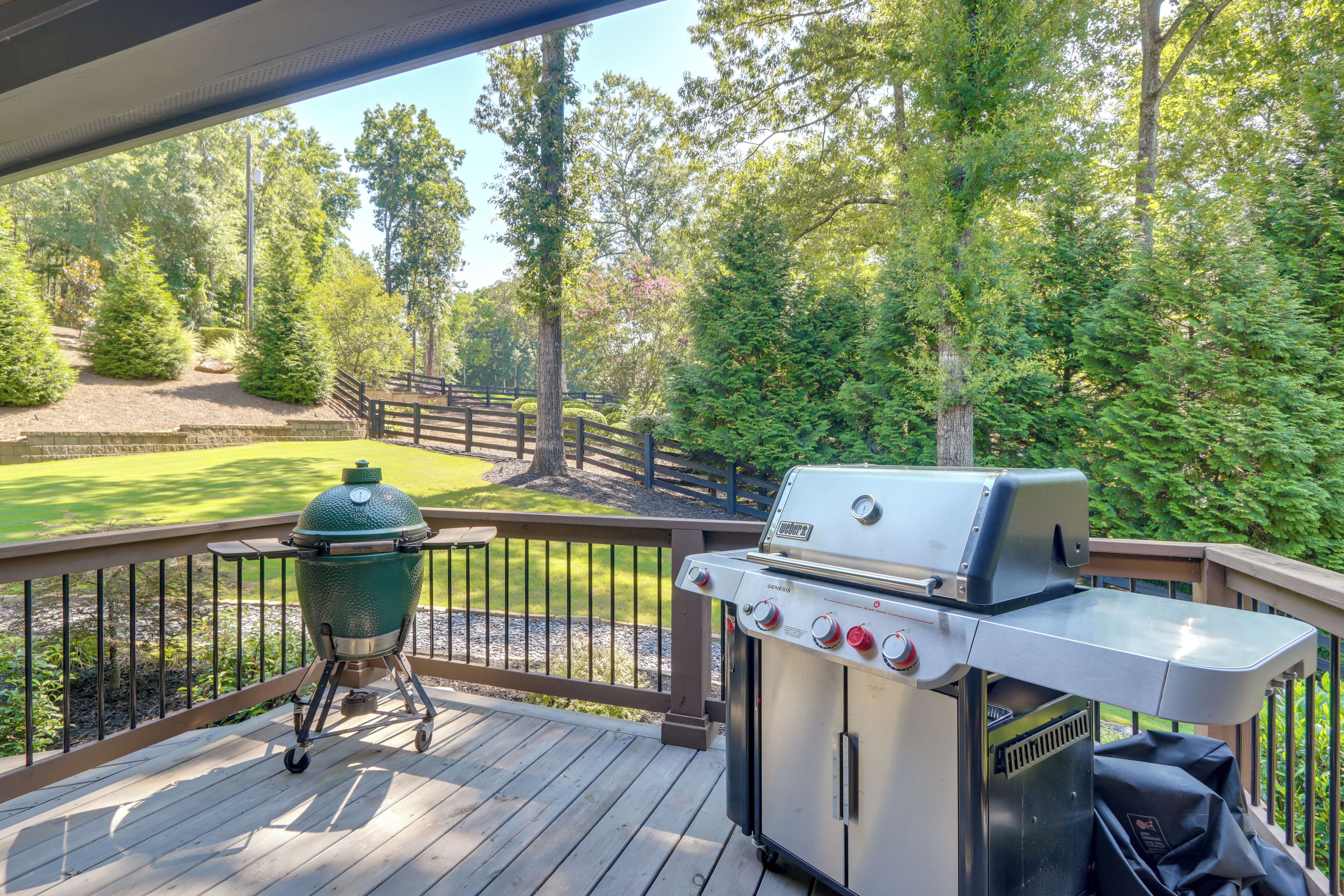 Una terrazza con una griglia Weber Genesis e un affumicatore, con vista su un prato curato e alberi.