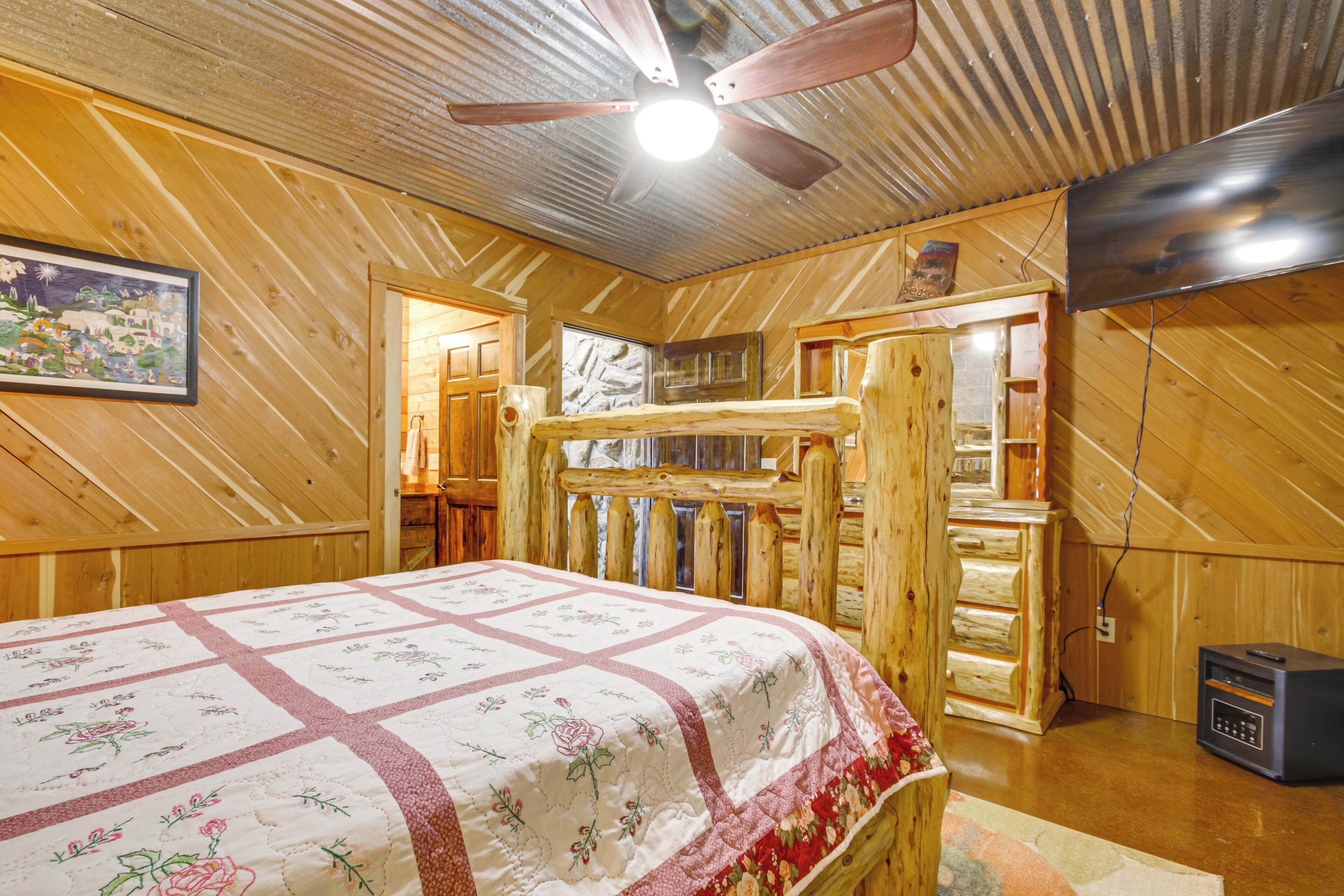 Interior de una cabaña de madera con cama, ventilador de techo y televisor.