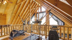Ein Holzinnenraum mit Deckenventilator, Trainingsgeräten und einem mit Vorhängen versehenen Fenster.
