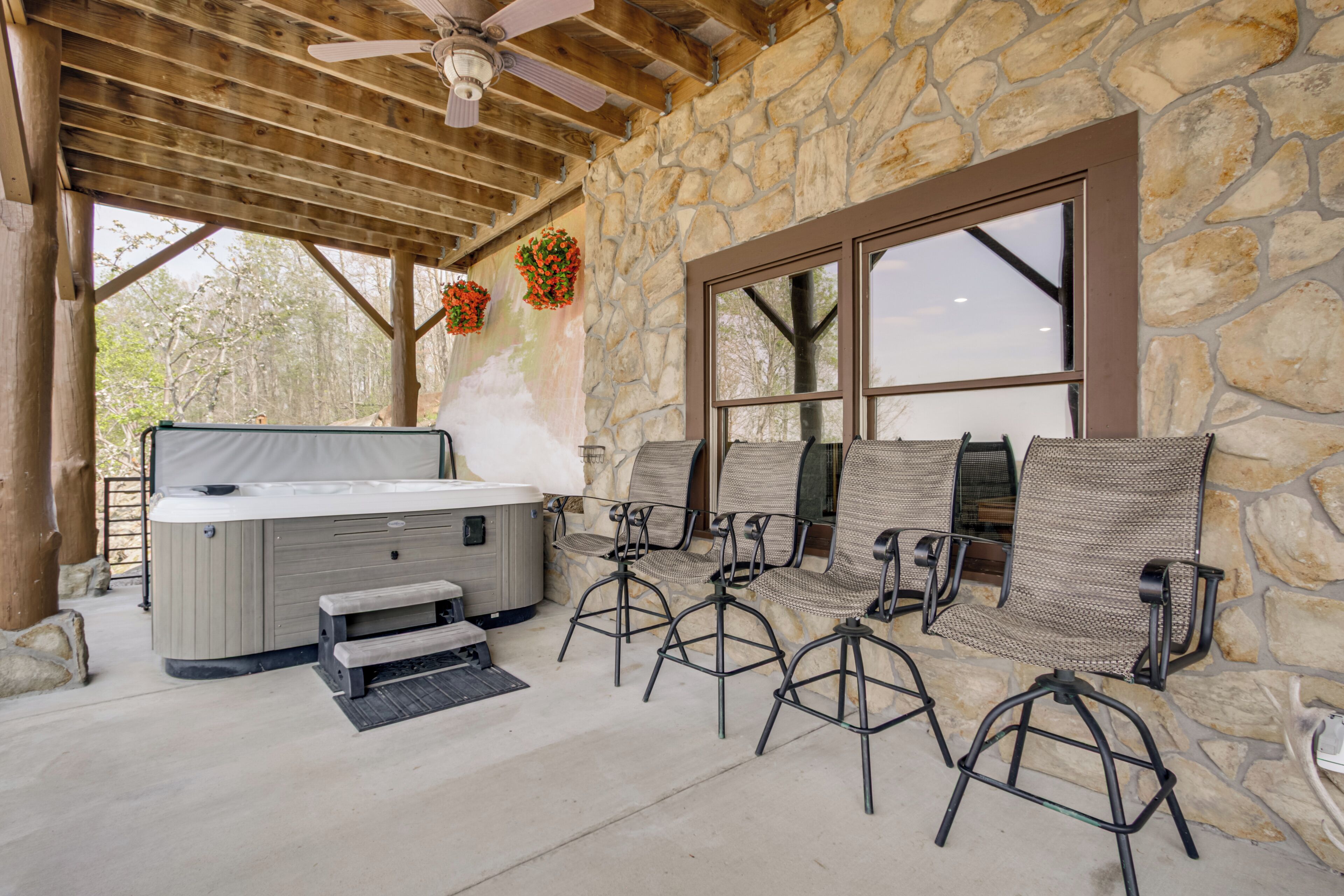 Un espacio al aire libre techado con paredes de piedra, un jacuzzi y mobiliario exterior.
