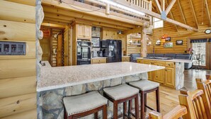 Ein Holzhütten-Interieur mit einer Kücheninsel aus Naturstein, Holzbarhocker, einer Küchenzeile und einem Balkon.