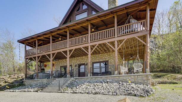 Eine zweistöckige Blockhütte mit Steinunterbau, einem Balkon mit Sitzgelegenheit und einem Steinkamin.