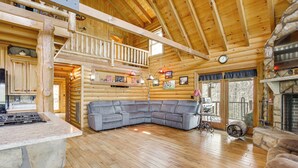 Ein Blockhaushaus-Interieur mit Kamin aus Stein, einem großen grauen Ecksofa und einer Küchenzeile.