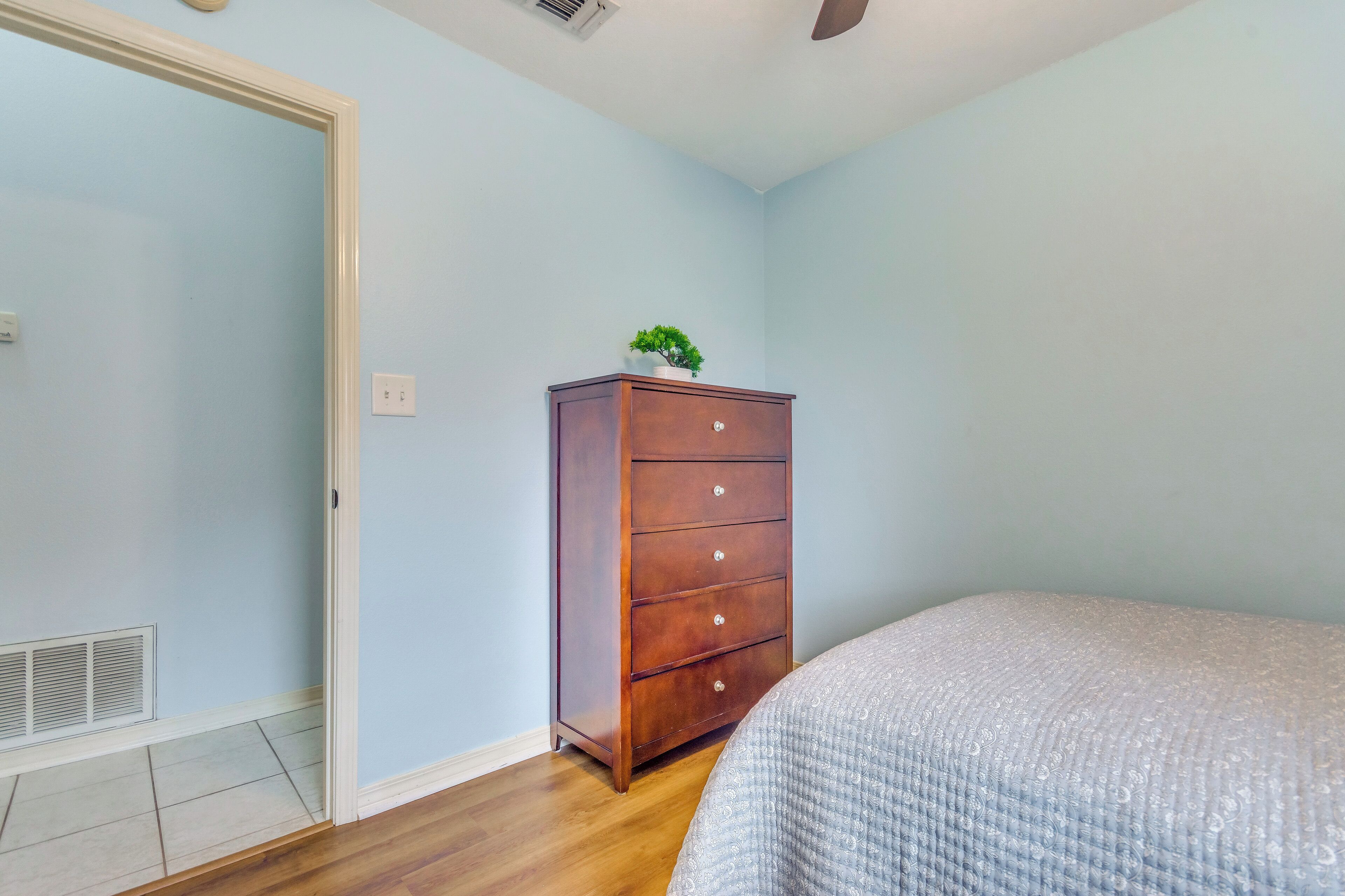 Un dormitorio con un aparador de madera, una cama y una pequeña planta encima del aparador.