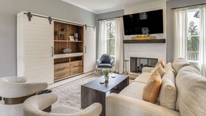 Ein Wohnzimmer mit einer Couch, Sesseln, einem Couchtisch, einem Fernseher, einem Kamin und einer Schiebetür im Bauernhausstil.