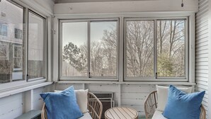 A room with a bench, two wicker chairs with cushions, a small round table, and large windows overlooking trees. - Walk to Beach! Serene Lake Michigan Home w/ Deck (Grand Haven)