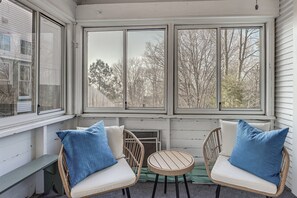 A room with a bench, two wicker chairs with cushions, a small round table, and large windows overlooking trees. - Walk to Beach! Serene Lake Michigan Home w/ Deck (Grand Haven)