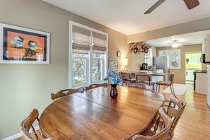 Uma sala de jantar com mesa e cadeiras de madeira, um vaso com flores e um quadro na parede.