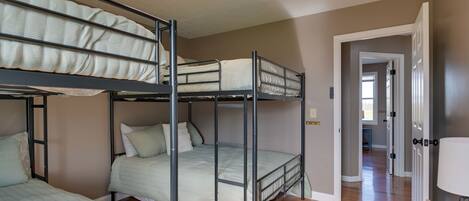 A bunk bed room with a ceiling fan, wooden flooring, and a hallway leading to another room.