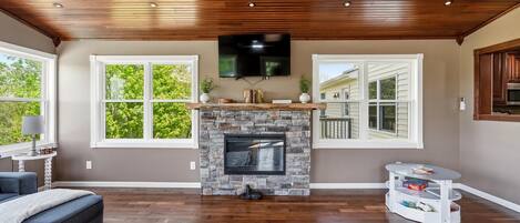 A living room with a stone fireplace, wooden ceiling, and large windows.