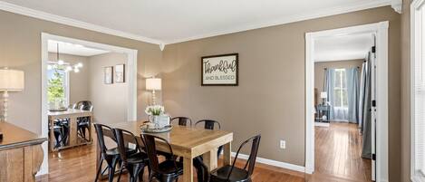 A dining area with a wooden table and black chairs, a kitchen in the background, and a hallway leading to another room.