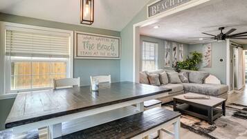 A dining area with a wooden table and benches, a ceiling fan, and a sign reading 'WELCOME TO OUR BEACH HOUSE.'