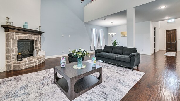A spacious living room with a fireplace, a dark wooden coffee table, a gray sofa, and a ceiling fan. - Near Lake & Family Fun! Spacious Oak Point Home (Little Elm)