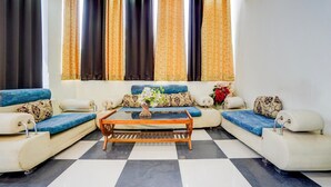 A living room with a sofa set, a coffee table, and a large window with curtains. - Classic Hotel Shimla Grand (Lucknow)