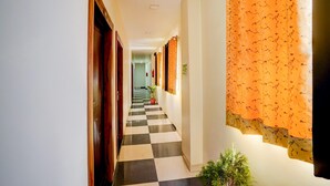 A corridor with checkered flooring, wooden doors, and orange patterned curtains. - Classic Hotel Shimla Grand (Lucknow)